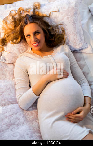 Hübsche junge schwangere Frau liegend auf dem Bett im Zimmer Stockfoto