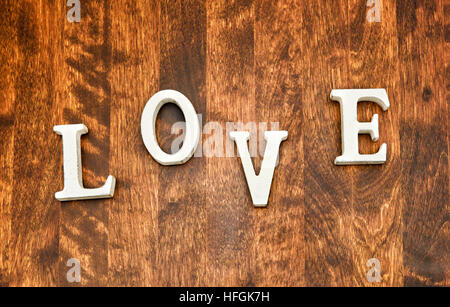 Wort "Liebe" auf hölzernen strukturierten Hintergrund. Die Buchstaben sind Hauptstädte und weiß in der Farbe. Hintergrund ist ein dunkler Broen Holz und seine Beschaffenheit ist klar Stockfoto