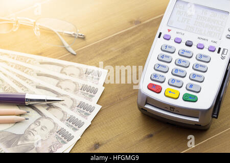 Kreditkarten-Terminal oder EDC auf Kasse Holztisch im Store mit japanischen Banknoten, Kugelschreiber, Bleistift und Taschenrechner. Stockfoto