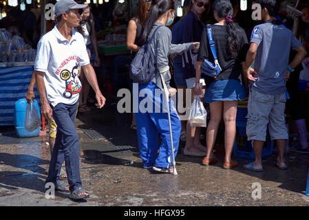 Mädchen auf Krücken, die Hilfe von anderen an einem belebten Marktstand anfordern. Thailand S. E. Asien Stockfoto