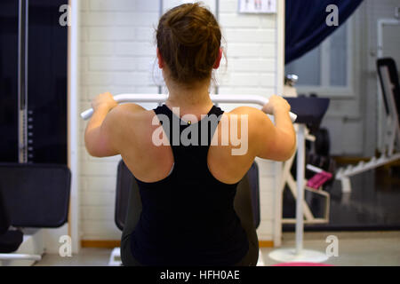 Frau, trainieren ihre Muskeln des Rückens und der Arme mit Riemenscheibe in der Turnhalle. Stockfoto