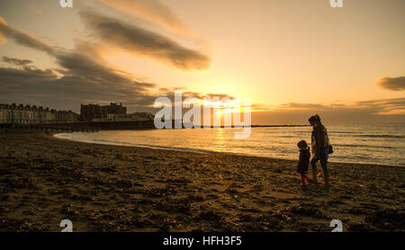 Aberystwyth Wales UK, New Years Eve, Samstag, 31. Dezember 2016 UK Wetter: Menschen zu Fuß am Strand beim Sonnenuntergang über dem Meer in Aberystwyth im Westen wales Küste am letzten Tag des Jahres. -Das Wetter im Westen war klar, in scharfem Kontrast zu der dichte Nebel, der über viel von Süd-Ost-England-Foto: Keith Morris / Alamy Live News Stockfoto