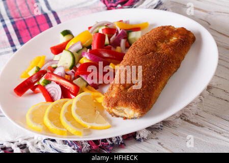 paniert gebratener Fisch mit frischem Gemüse und einer Zitrone auf einem Teller. horizontale Stockfoto