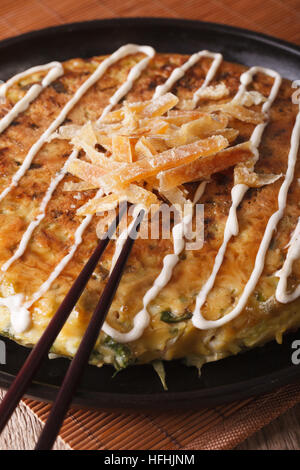 Japanische Pizza: Okonomiyaki auf eine Platte Nahaufnahme und Stäbchen. Vertikal Stockfoto
