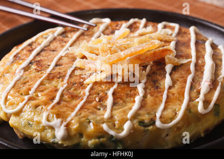 Japanisches Essen: Okonomiyaki auf einer Platte Makro- und Stäbchen. horizontale Stockfoto