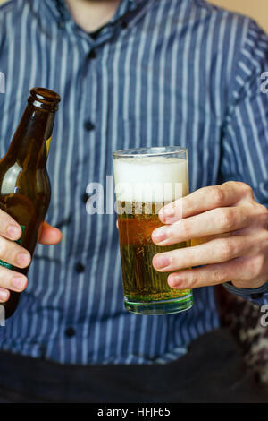 Junger Mann hält eine Flasche und einem Glas blondes Bier Stockfoto