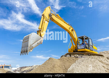 Gelbe Bagger macht Flor des Bodens durch Hochziehen Boden auf Heap auf Baustelle, Projekt im Gange. Stockfoto