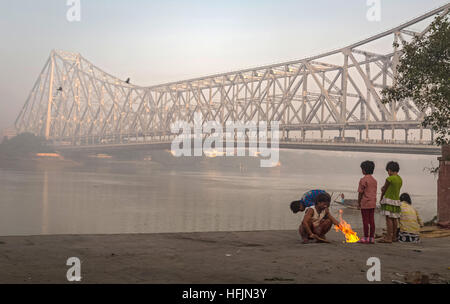 Straßenkinder halten an einem kalten nebligen Wintermorgen auf Mallick Ghat in der Nähe von Howrah Brücke am Ufer des Fluss Hooghly warm. Stockfoto