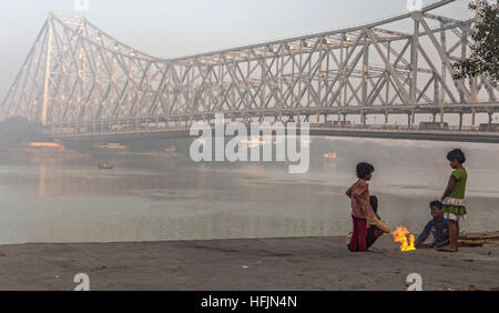 Straßenkinder halten an einem kalten nebligen Wintermorgen auf Mallick Ghat in der Nähe von Howrah Brücke am Ufer des Fluss Hooghly warm. Stockfoto