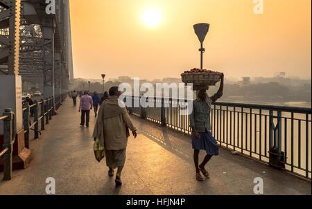 Anbieter und Pendler überqueren Howrah Brücke am Fluss Hooghly auf einem kalten, nebligen Wintermorgen für ihre täglichen Aktivitäten. Stockfoto