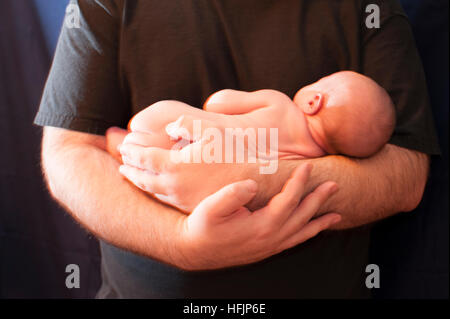 Neugeborenes Baby in den Armen des Vaters schläft, sein Gesicht ist nicht vollständig sichtbar. Stockfoto