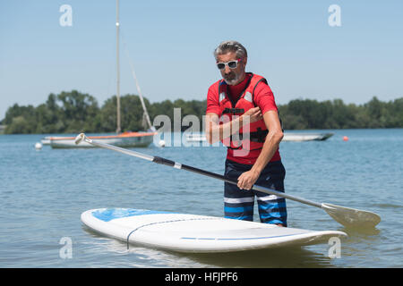 Mann neben einem Stand up Paddle Board auf dem See Stockfoto