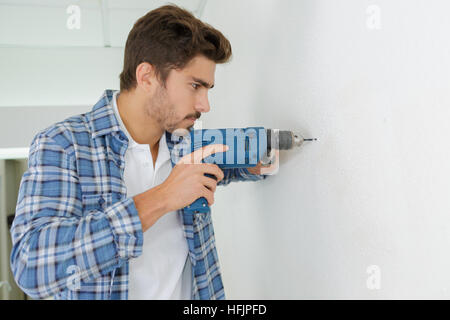 männliche Baumeister Bohren von Löchern in der Wand auf Baustelle Stockfoto
