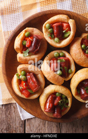 Yorkshire Pudding gefüllt mit Wurst und grüne Erbsen auf einem Teller mit einer Tabelle Großaufnahme. vertikale Ansicht von oben Stockfoto