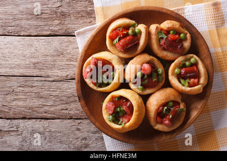 Yorkshire Pudding gefüllt mit Wurst und grüne Erbsen auf einem Teller auf den Tisch. horizontale Ansicht von oben Stockfoto