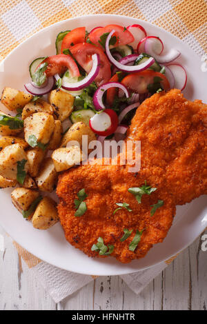 Wiener Schnitzel, Bratkartoffeln und Salat auf den Tisch-Nahaufnahme. vertikale Ansicht von oben Stockfoto