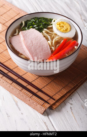 Ramen-Nudeln in Brühe mit Schweinefleisch, Gemüse und Ei in eine Schüssel geben. vertikale Stockfoto