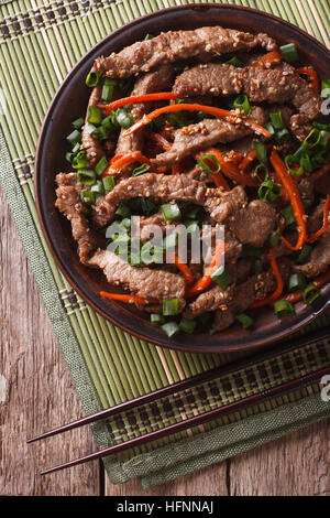 Asiatische Küche: Bulgogi Rindfleisch Scheiben gebraten mit Sesam und Karotte Nahaufnahme auf einer Platte. vertikale Ansicht von oben Stockfoto