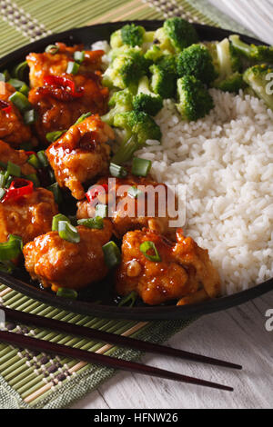 General Tso Chicken mit Reis, Zwiebeln und Brokkoli Nahaufnahme auf einer Platte. vertikale Stockfoto