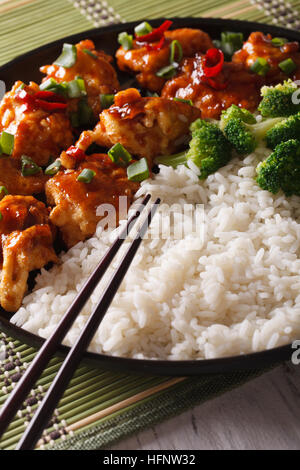 Asiatische Küche: Huhn in Soße mit Reis und Broccoli Nahaufnahme auf einer Platte. vertikale Stockfoto