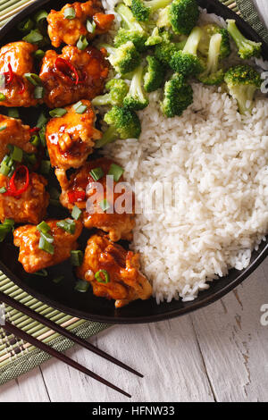 Asiatische Küche: Hähnchen Tso in Soße mit Reis und Broccoli Nahaufnahme auf einer Platte. vertikale Ansicht von oben Stockfoto