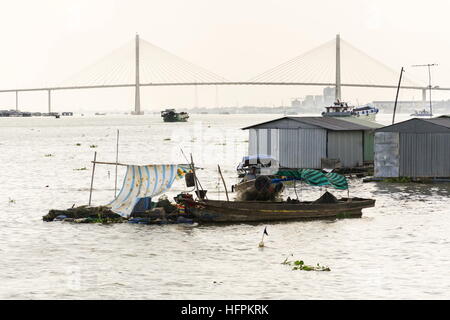 Mann fährt auf ratty Boot mit Fischzucht Floß-Haus schwimmt auf Mekong Fluss mit Rach Mieu Brücke in My Tho, Vietnam. Stockfoto