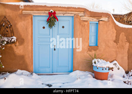 Eine gealterte blau Holztür mit einem Ast der Kiefer auf einer Adobe-Stil Haus in Taos, New Mexico. Stockfoto