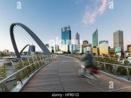 Radfahrer der Elizabeth Quay-Brücke in der Dämmerung mit der Skyline der Stadt darüber hinaus, Perth, Western Australia, Australien Stockfoto
