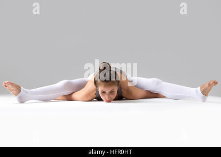 Junge Frau in Kurmasana Pose, grau Studio-Hintergrund Stockfoto