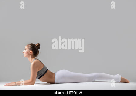 Junge Frau im Ardha Bhudjangasana pose, graue Studio-Hintergrund Stockfoto