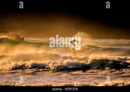 Ein Surfer reitet eine wilde Welle während einer goldenen Sonnenuntergang am Fistral Beach in Newquay, Cornwall. Surfer in Aktion. UK. Stockfoto
