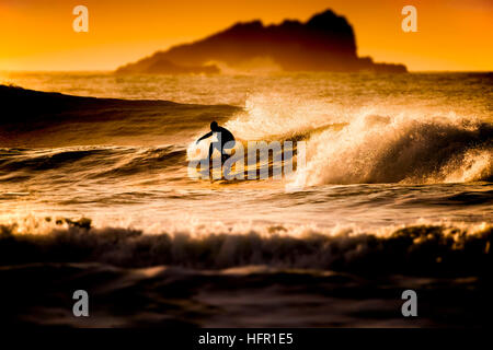 Ein Surfer auf einer Welle in einem goldenen Sonnenuntergang am Fistral in Newquay, Cornwall.  Surfer in Aktion. VEREINIGTES KÖNIGREICH. Stockfoto