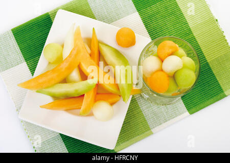 Melone Keile auf einem Teller neben Schüssel mit Melonenkugeln Stockfoto