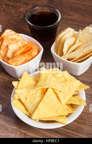 Haufen von knackigen gesalzene Kartoffelchips und Cookies in Schalen, Glas Cola, Begriff der Beschränkung ungesund und gesalzenem Essen Stockfoto