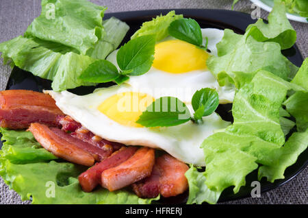 Spiegeleier mit Kräuter, Salat und Scheiben von gebratenem Speck auf eine Platte Nahaufnahme mit geringer Tiefe des Fokus Stockfoto