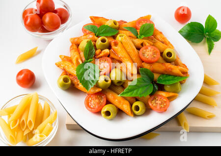 Weißen Teller mit Penne-Nudeln mit Cherry-Tomaten, Oliven und Kräutern auf einem Holztablett dekoriert Stockfoto