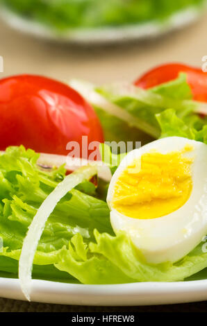 Gekochtem Ei, Salat und saftige rote Kirsche mit Zwiebeln auf eine Platte Nahaufnahme in Soft-Fokus im Hintergrund Stockfoto