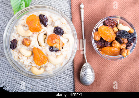 Draufsicht auf eine Portion Haferflocken mit Obst und Beeren in eine Glasschüssel zum Frühstück auf eine graue Tischdecke Stockfoto