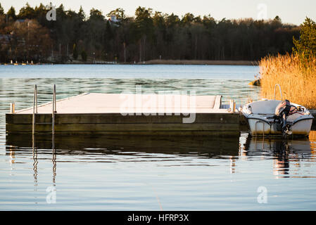 Kleines Boot mit Außenbordmotor zu einem Frost gebissen Schwimmsteg im regungslosen Wasser gebunden. Ort Ronneby in Südschweden. Stockfoto