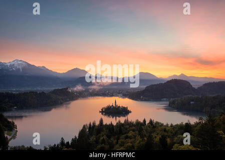 Blick über Bleder See bei Sonnenaufgang mit der Insel mit der Kirche und Reflexion von den bunten Himmel im See in Slowenien. Stockfoto