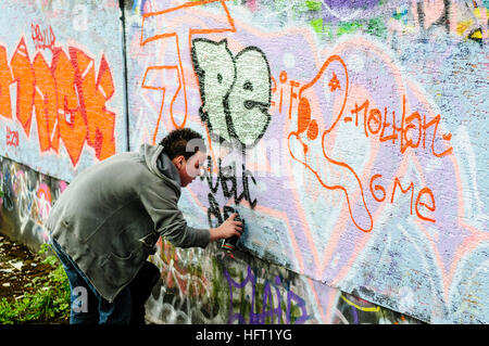 Ein Jugendlicher verwendet Sprühlack Graffiti an der Wand zu zeichnen. Stockfoto