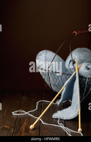 Stricken von leichten blauen Garn auf dunklem Braun aus Holz. Stockfoto