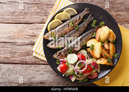 Gegrillte Sardinen mit Bratkartoffeln und Salat aus frischem Gemüse Nahaufnahme auf einer Platte. Horizontale Ansicht von oben Stockfoto