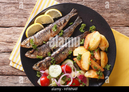 Gebratene Sardinen mit Kartoffeln und Salat aus frischem Gemüse Nahaufnahme auf einer Platte. horizontale Ansicht von oben Stockfoto