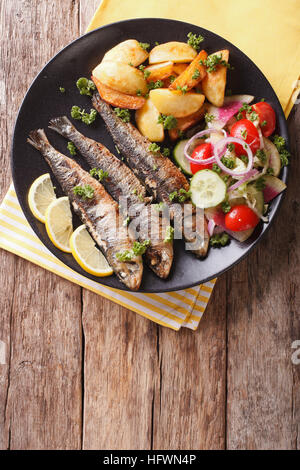 Gegrillte Sardinen mit Bratkartoffeln und Salat aus frischem Gemüse Nahaufnahme auf einer Platte. vertikale Ansicht von oben Stockfoto