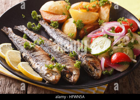 Gebratene Sardinen mit Kartoffeln und Salat aus frischem Gemüse Nahaufnahme auf einer Platte. horizontale Stockfoto