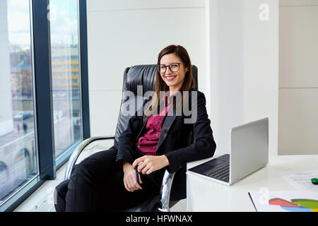 Business-Frau lächelnd hinter einem Schreibtisch im modernen Büro an windo Stockfoto