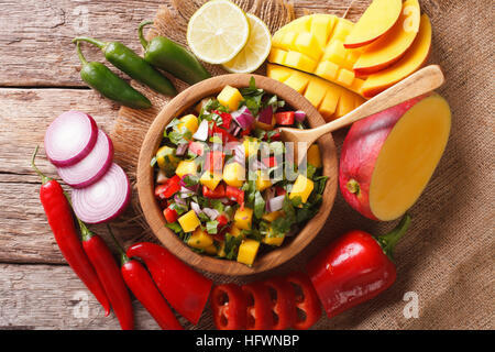 Mexikanisches Essen: Salsa mit Mango, Koriander, Zwiebeln und Paprika hautnah in eine Schüssel geben und die Zutaten auf den Tisch. Horizontale Ansicht von oben Stockfoto