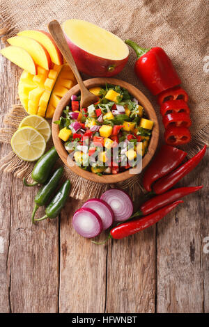 Mexikanisches Essen: Salsa mit Mango, Koriander, Zwiebeln und Paprika hautnah in eine Schüssel geben und die Zutaten auf den Tisch. vertikale Ansicht von oben Stockfoto