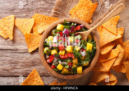 Mexikanische Salsa mit Mangos, Paprika, Koriander und Zwiebeln in einer Schüssel und Mais-Chips auf dem Tisch hautnah. Horizontale Ansicht von oben Stockfoto